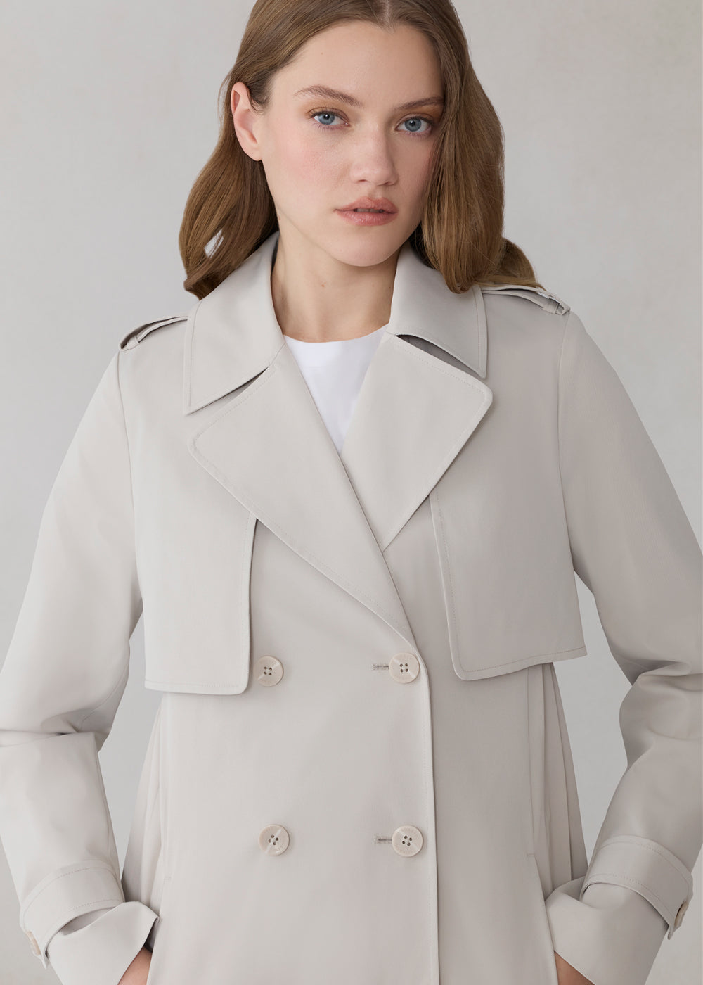 Woman wearing a light oak trench coat against a plain background